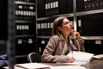 Manager talking at landline phone with remote bookkeeper, discussing accountancy report in storage room. Businesswoman working late at night at administrative catalog in corporate depository - obrazy, fototapety, plakaty