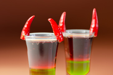 Layered drink shot prepared with vodka, green liquor, grenadine and lemon juice decorated with bird eye chillies in the shape of horns