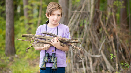 happy 10 year old boy on a hike, in a camp, holding a fire yard. a joyful child holds branches for...