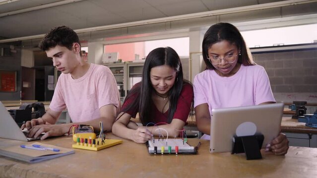 Group of three young students from a technical high school doing a technological team project. People using the computer consulting doubts about their practices in electronic technology class.