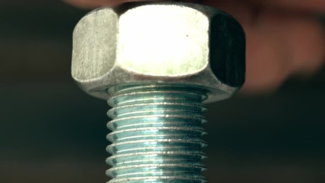 Man's hand is screwing a huge nut onto a large shiny metal screw with thread closeup. 4K real time video.