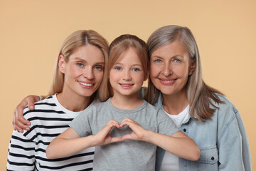Three generations. Happy grandmother, her daughter and granddaughter making heart with hands on beige background