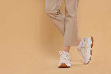 Woman wearing pair of new stylish sneakers on beige background, closeup. Space for text - Powered by Adobe