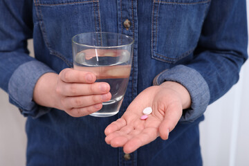 Woman with glass of water and pill on blurred background, closeup
