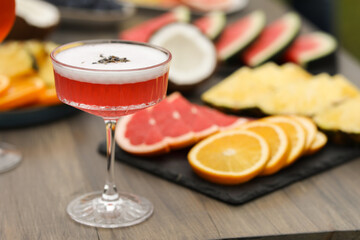 Glass of cocktail and fruits on wooden table, closeup
