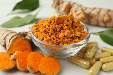 Aromatic turmeric powder, pills and raw roots on white table, closeup