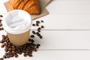 Coffee to go. Paper cup with tasty drink, croissant and beans on white wooden table. Space for text