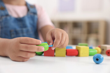 Motor skills development. Little girl playing with wooden pieces and string for threading activity at table indoors, closeup