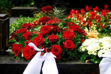 a bouquet of funeral flowers from red roses with white mourning bow on a grave after a funeral