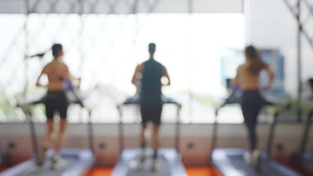Group of athletic men and women running on treadmill at fitness gym. Blurred focused