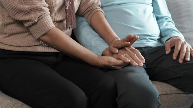 Close up view of senior couple holding hands while sitting on the sofa in the living room together.
