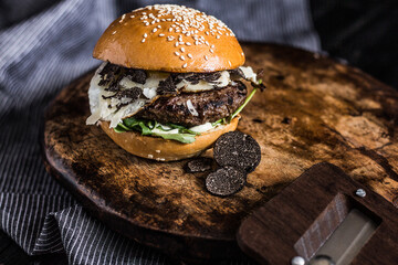Close-up of truffle burger with fried egg decorated on a wooden plate and dark background,...