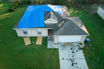 Hurricane Ian damaged house rooftop covered with protective plastic tarp against rain water leaking...
