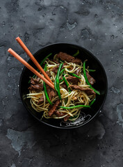 Udon noodles with beef and green string beans on a dark background, top view