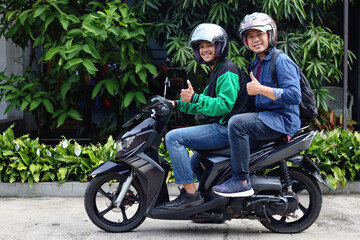 Back view of happy commercial motorcycle taxi driver and his passenger showing thumb up