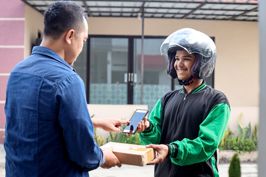 Asian deliverman holding a package and phone, delivery to male customer. Motorbike delivering parcel express service concept.