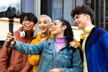 Obraz premium Female college student influencer vlogging with friends outdoors. Group of teenagers vlogging with camera in the street.