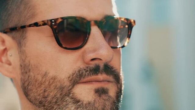 Handsome confident stylish hipster lambersexual model. modern man dressed in elegant blue shirt. Fashion male posing in the street background in Europe city at sunset. In sunglasses