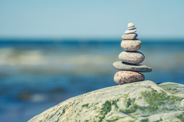 Balancing stones on a big rock with sea grass on the beach, with blue water waves on background, Baltic Sea, Olando Kepure, Lithuania