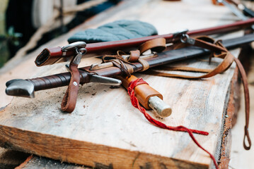 Medieval weapon swords in scabbards lying on a wooden board in the open air, close-up