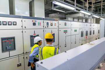 Professional electrical engineer in safety uniform working at factory server electric control panel...