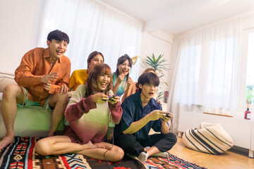 Group of Young Asian man and woman playing video games together in living room at home. Happy people friends enjoy and fun indoor activity lifestyle spending time together on holiday vacation.