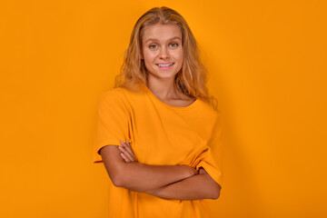 Obraz premium Young confident beautiful Caucasian woman blonde stands with arms crossed and looks at camera with smile demonstrating positive emotions and self-confidence posing on isolated yellow background.