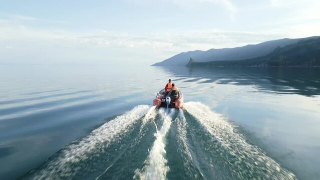 The motor boat is moving at speed on Lake Baikal against the backdrop of beautiful landscapes of rocks. The view from the drone. The sky is reflected in the surface of the water
