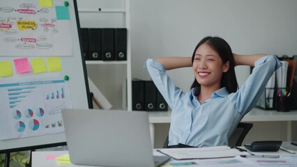 Young adorable Asian businesswoman stretching after working with laptop in her office room.