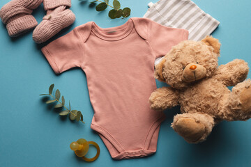 Flat lay of pink baby grow, hat, teddy bear and pink booties with copy space on blue background