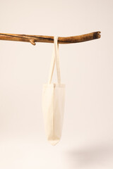 White canvas bag hanging from wooden branch with copy space on white background