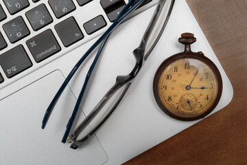 Vintage pocket watch on a laptop and a pair of eye glasses 
