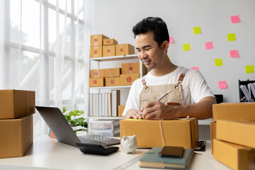 Man writing on parcel box, online shop owner checking orders from website on internet to confirm order with customers who ordered and pack products for delivery. Concept of selling products online.