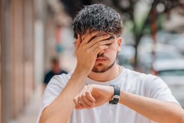 young man looking at watch scared on the street, punctuality - obrazy, fototapety, plakaty