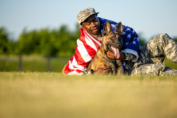 True American heroes. Soldier in uniform lying on the grass with his military dog covered in USA flag.