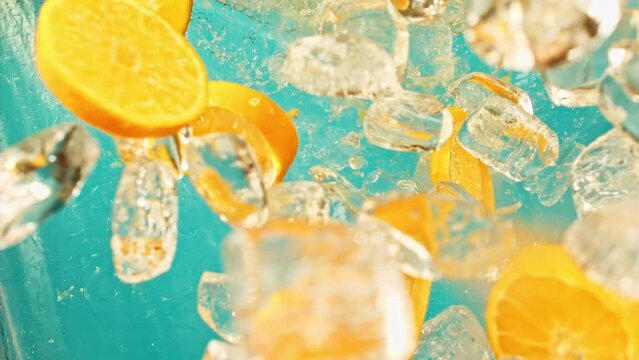 Fresh juicy orange and juice, ice cube and water drops splash pours in super slow motion 1000 fps. Citrus orange slices and ice cube fly or fall on blue background, slow motion vertical or horizontal