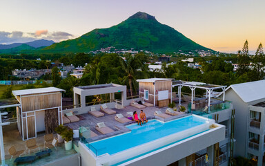 Men and Woman watching sunrise by a swimming pool, a couple on a honeymoon vacation in Mauritius with on the background the Tamarin mountain