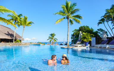 Man and Woman relaxing in a swimming pool, a couple on a honeymoon vacation in Mauritius tanning in the pool with palm trees and sun beds