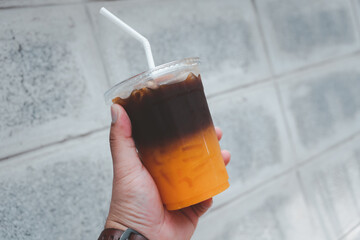 A glass of coffee mix orange juice with ice in young hand on a cement background.