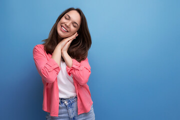 charming smiling brunette young woman in a pink shirt and jeans on a studio isolated background