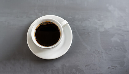 Black coffee in a white mug on a saucer on a grey table. Copy space.