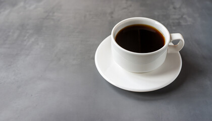 Black coffee in a white mug on a saucer on a grey table. Copy space.