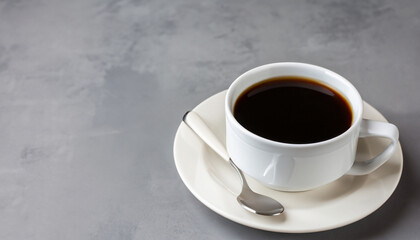 Black coffee in a white mug on a saucer on a grey table. Copy space.