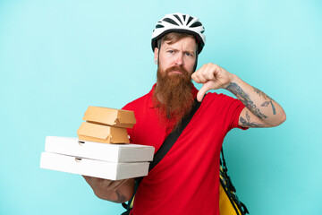 Delivery man holding pizzas and burgers isolated on blue background showing thumb down with...