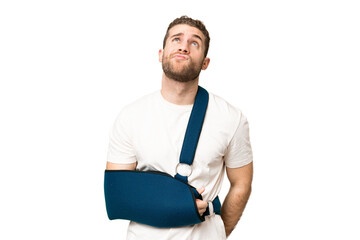 Young handsome blonde man with broken arm and wearing a sling over isolated chroma key background and looking up