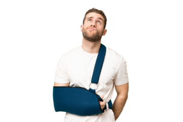 Young handsome blonde man with broken arm and wearing a sling over isolated chroma key background and looking up