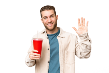 Young handsome blonde man holding soda over isolated chroma key background saluting with hand with happy expression