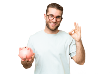 Young man holding a piggybank over isolated chroma key background showing ok sign with fingers