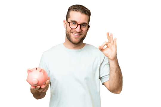Young man holding a piggybank over isolated chroma key background showing ok sign with fingers