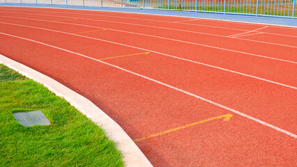 Empty red curve synthetic running tracks and green field in athletic outdoors stadium